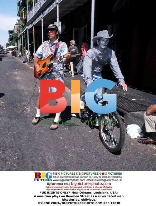 Musician plays on Bourbon Street as silver-faced man bikes by